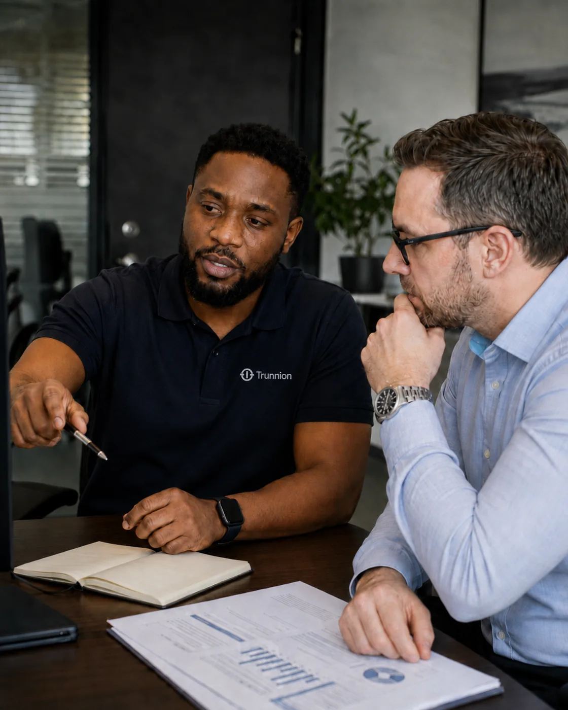 A Trunnion engineer sitting alongside a client at a desk, pointing out a
                    figure on a printed report.