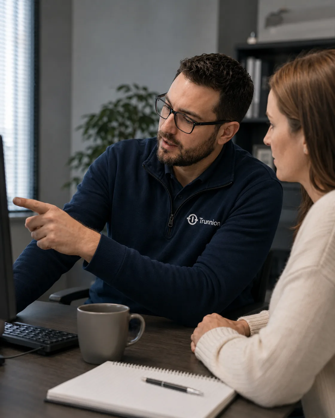 A Trunnion engineer at a desk with a client, pointing at a screen while
                    they talk through it together.